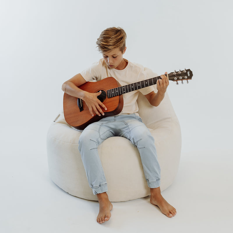 boy playing guitar in a cream plush lounger bean bag