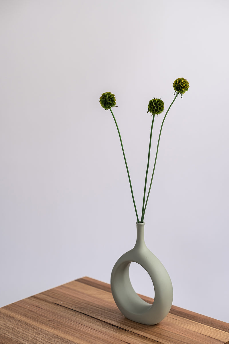 modern sage ceramic vase with dried flowers on a wooden shelf